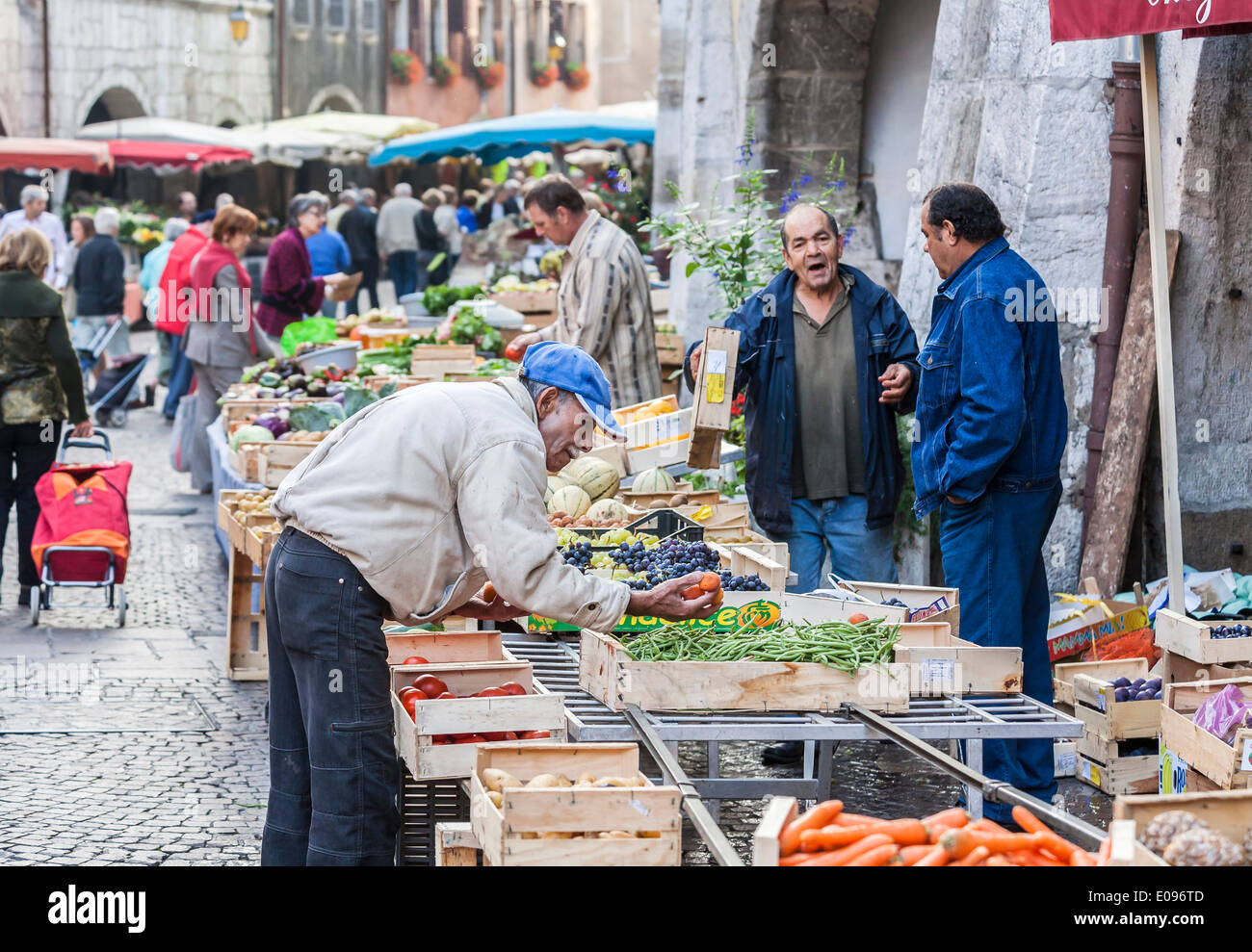 Stile di vita: Un anziano francese ispeziona i prodotti in una trafficata bancarella locale di mercato ortofrutticolo all'aperto ad Annecy, in Francia, mentre gli stallholder parlano Foto Stock