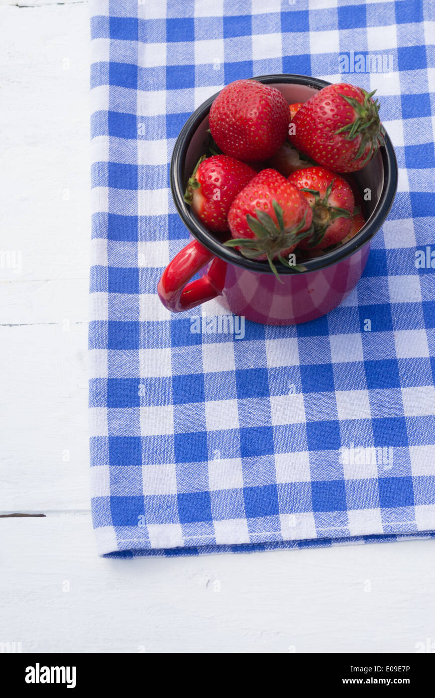 Un piccolo rosso vaso riempito con le fragole su un blu e bianco a scacchi in canovaccio. Foto Stock