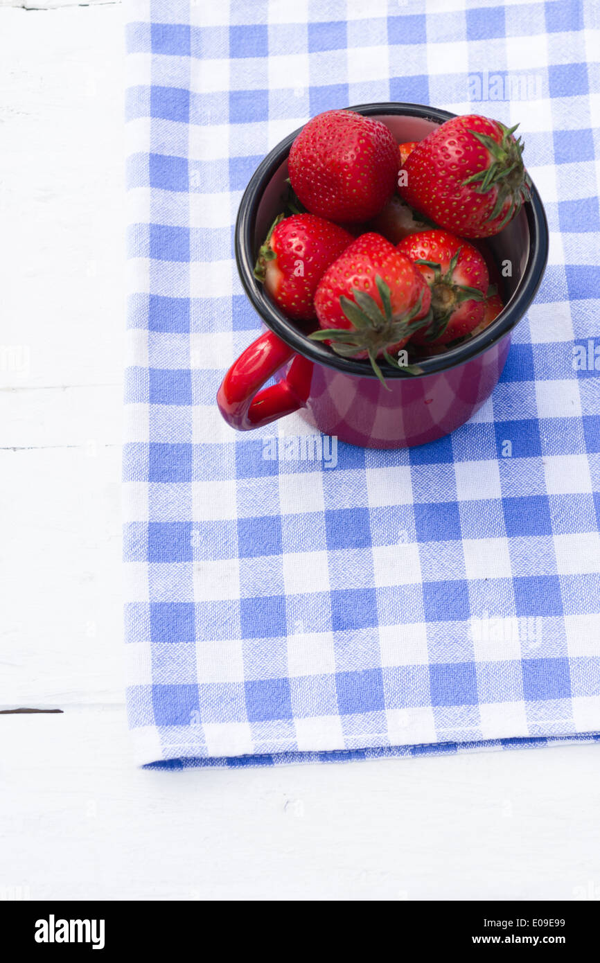 Un piccolo rosso vaso riempito con le fragole su un blu e bianco a scacchi in canovaccio. Foto Stock