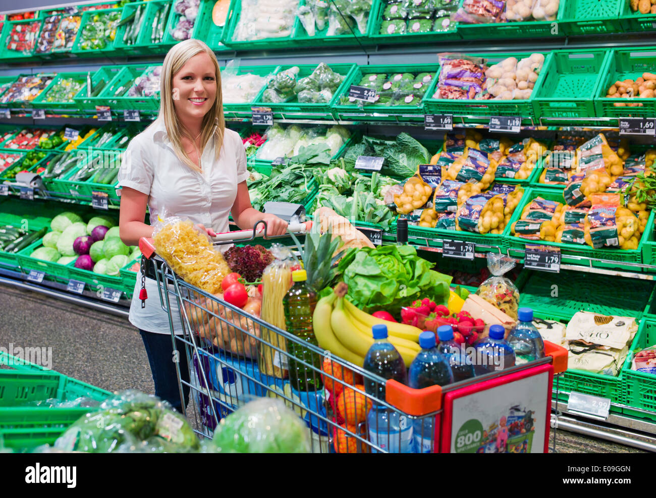 Una giovane donna con fare acquisti al supermercato. Full shopping cart., Eine junge Frau beim einkaufen im Supermarkt. Voller Foto Stock