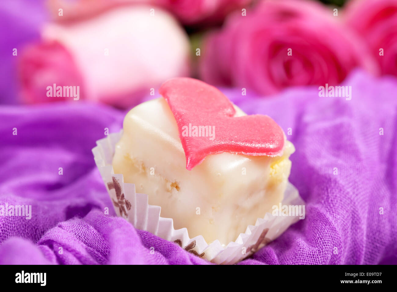 Petit Four decorate con cuore di marzapane sul panno viola Foto Stock