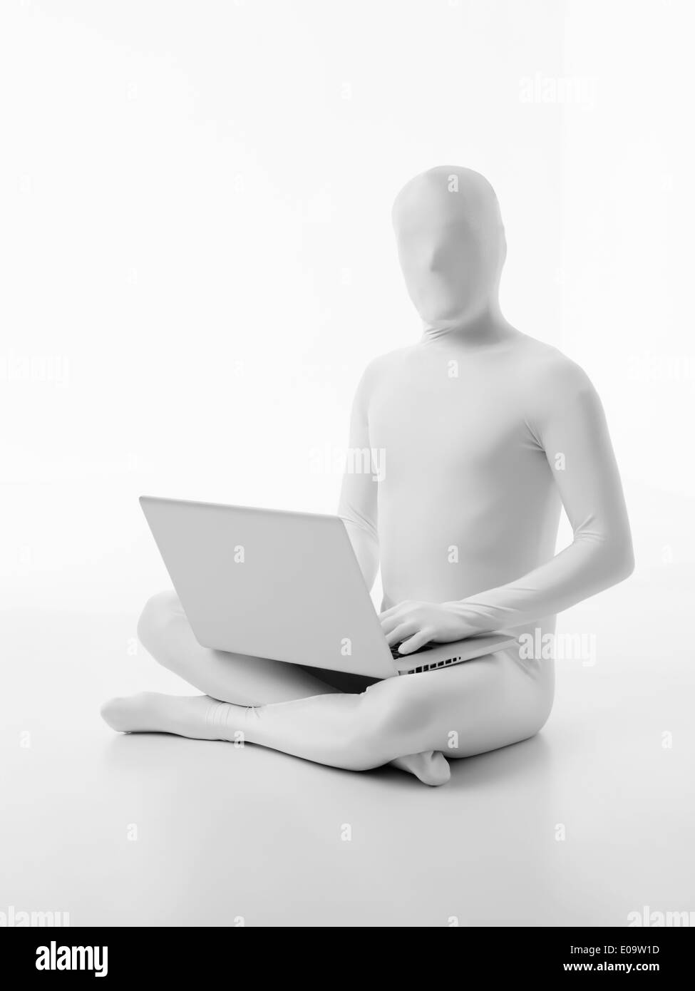 L'uomo senza volto vestito di bianco seduto con un computer portatile in giro la digitazione Foto Stock
