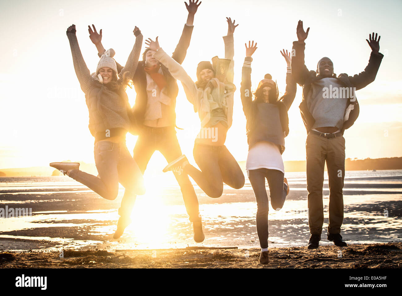 Cinque amici adulti jumping metà aria sulla spiaggia Foto Stock