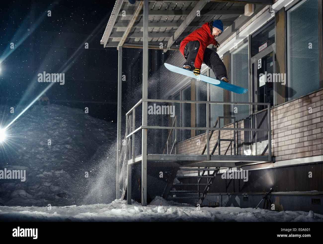 Metà maschio adulto snowboarder jumping metà aria dalla costruzione di notte Foto Stock