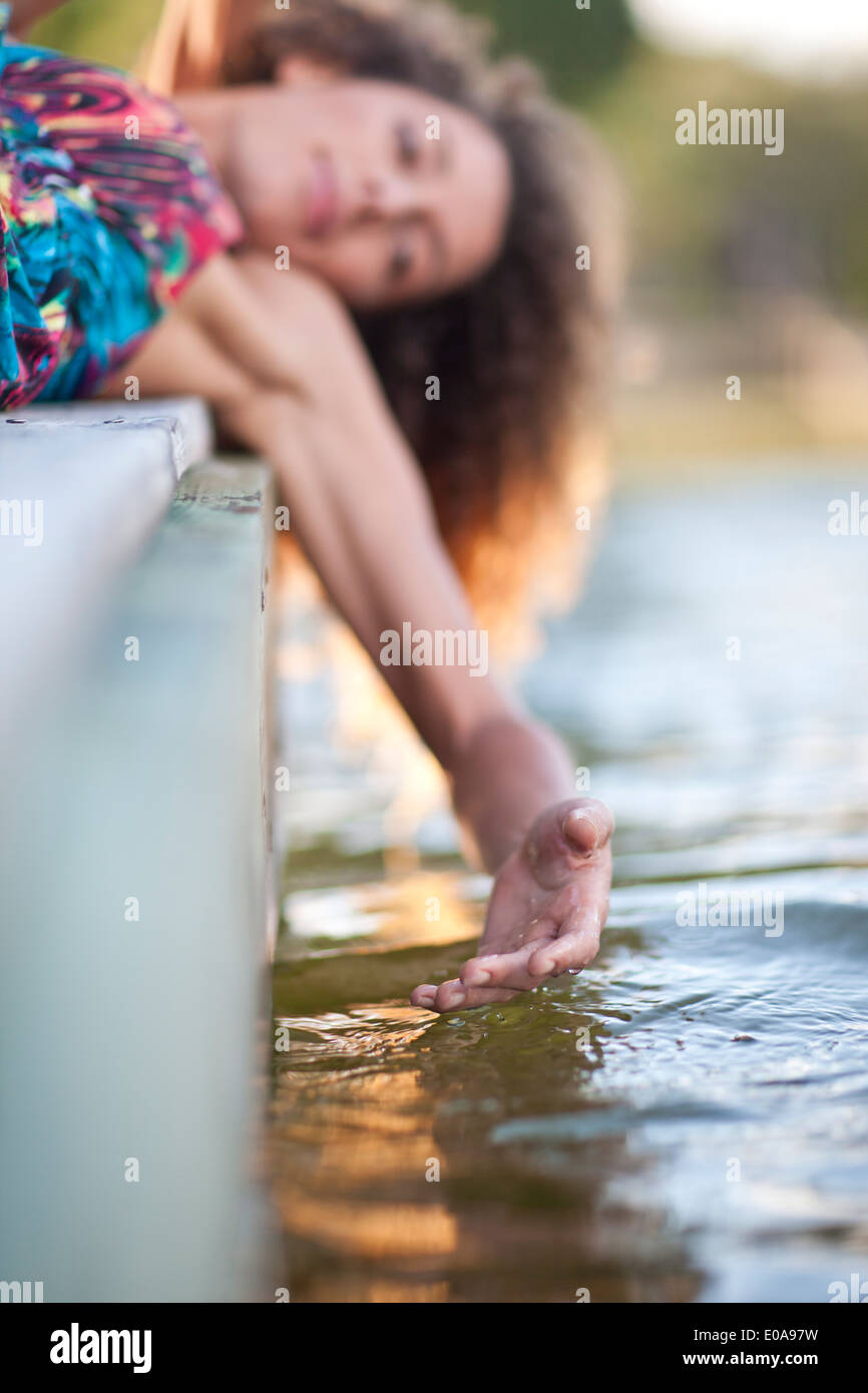 Giovane donna posa su jetty, mano toccare acqua Foto Stock