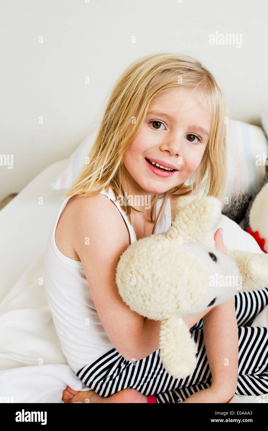 Ritratto di giovane ragazza inginocchiata sul letto con giocattolo morbido Foto Stock