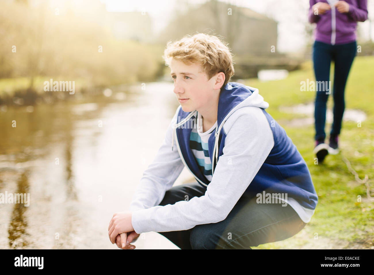 Infelice ragazzo adolescente accovacciato sul lungofiume Foto Stock