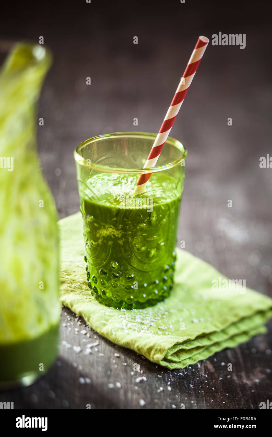 Bicchiere di frullato di spinaci con latte di cocco, limone e succo di arancia e banana sul tovagliolo e tavolo in legno Foto Stock