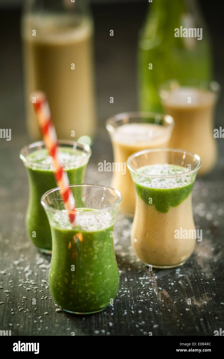 Bicchieri di frullato di spinaci e mango smoothie con noce di cocco essicata su un tavolo di legno Foto Stock