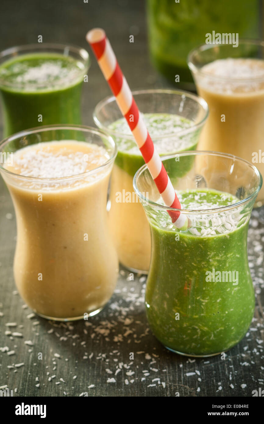 Bicchieri di frullato di spinaci e mango smoothie con noce di cocco essicata su un tavolo di legno Foto Stock