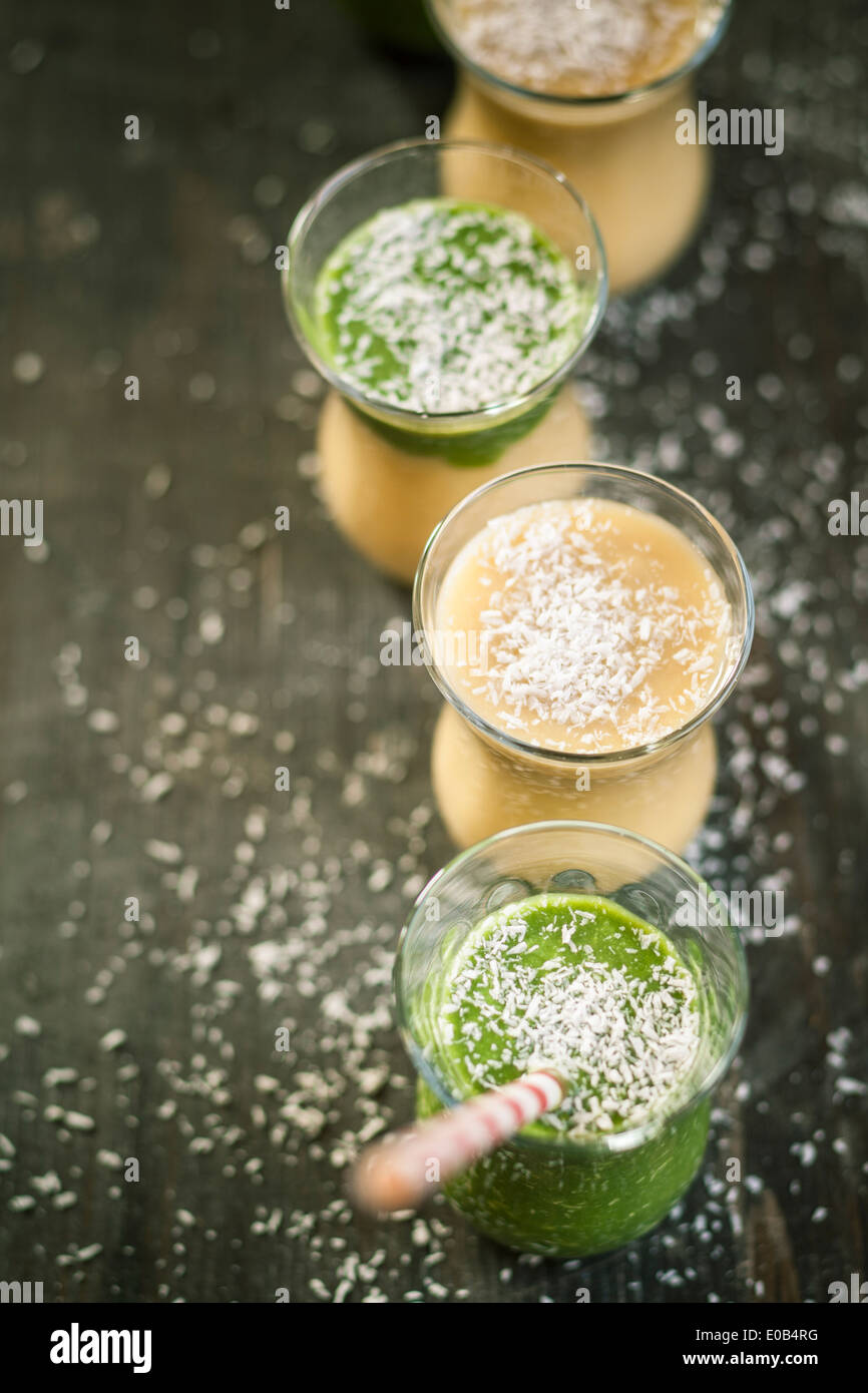 Bicchieri di frullato di spinaci e mango smoothie con noce di cocco essicata su un tavolo di legno, vista in elevazione Foto Stock