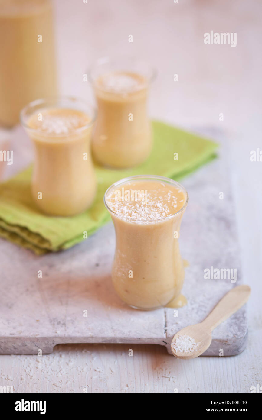 Bicchieri di mango smoothie con noce di cocco essicata su stoffa e scheda di cucina Foto Stock