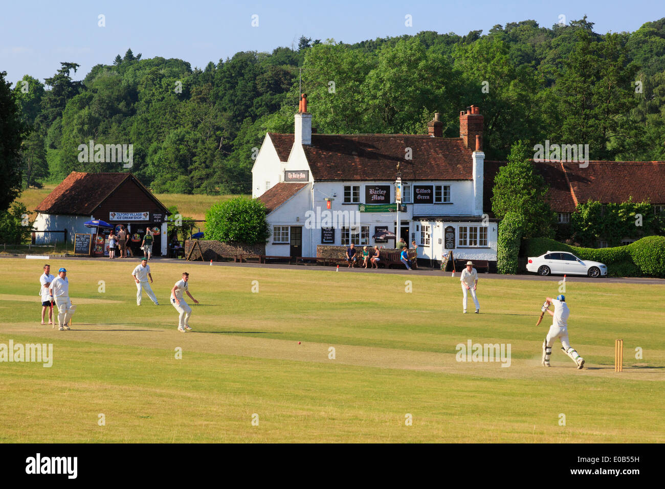 Le squadre locali giocando una partita di cricket su un villaggio verde nella parte anteriore di orzo Mow pub in una sera d'estate. Tilford Surrey in Inghilterra REGNO UNITO Foto Stock