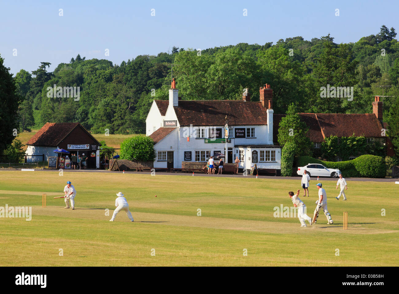Country LIFE squadre locali che giocano una partita di cricket su un villaggio verde di fronte al pub Barley Mow in una serata estiva. Tilford Surrey Inghilterra Regno Unito Foto Stock