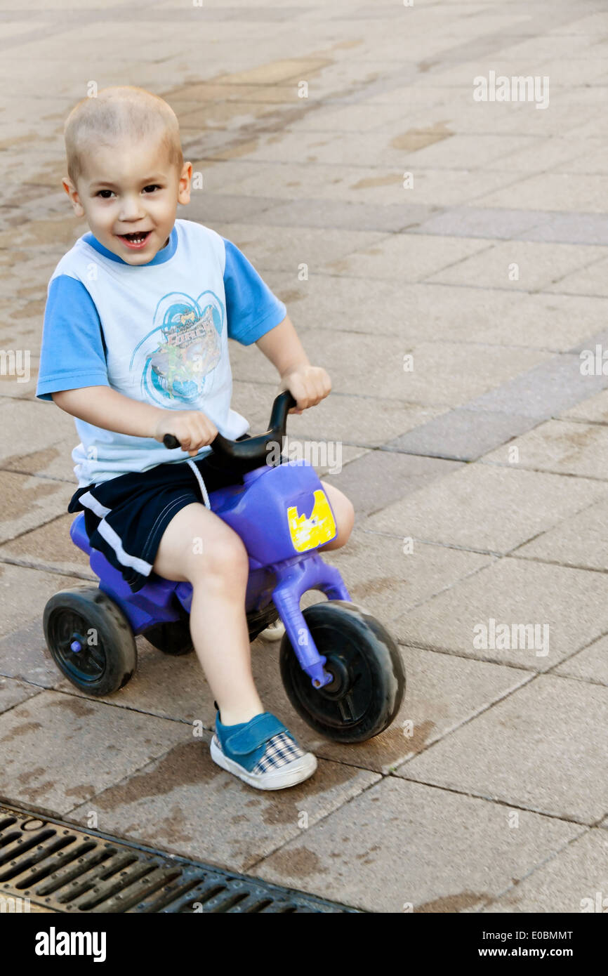Un piccolo bambino con il suo triciclo, Ein kleines tipo faehrt froehlich mit seinem Dreirad auf einem Platz Foto Stock