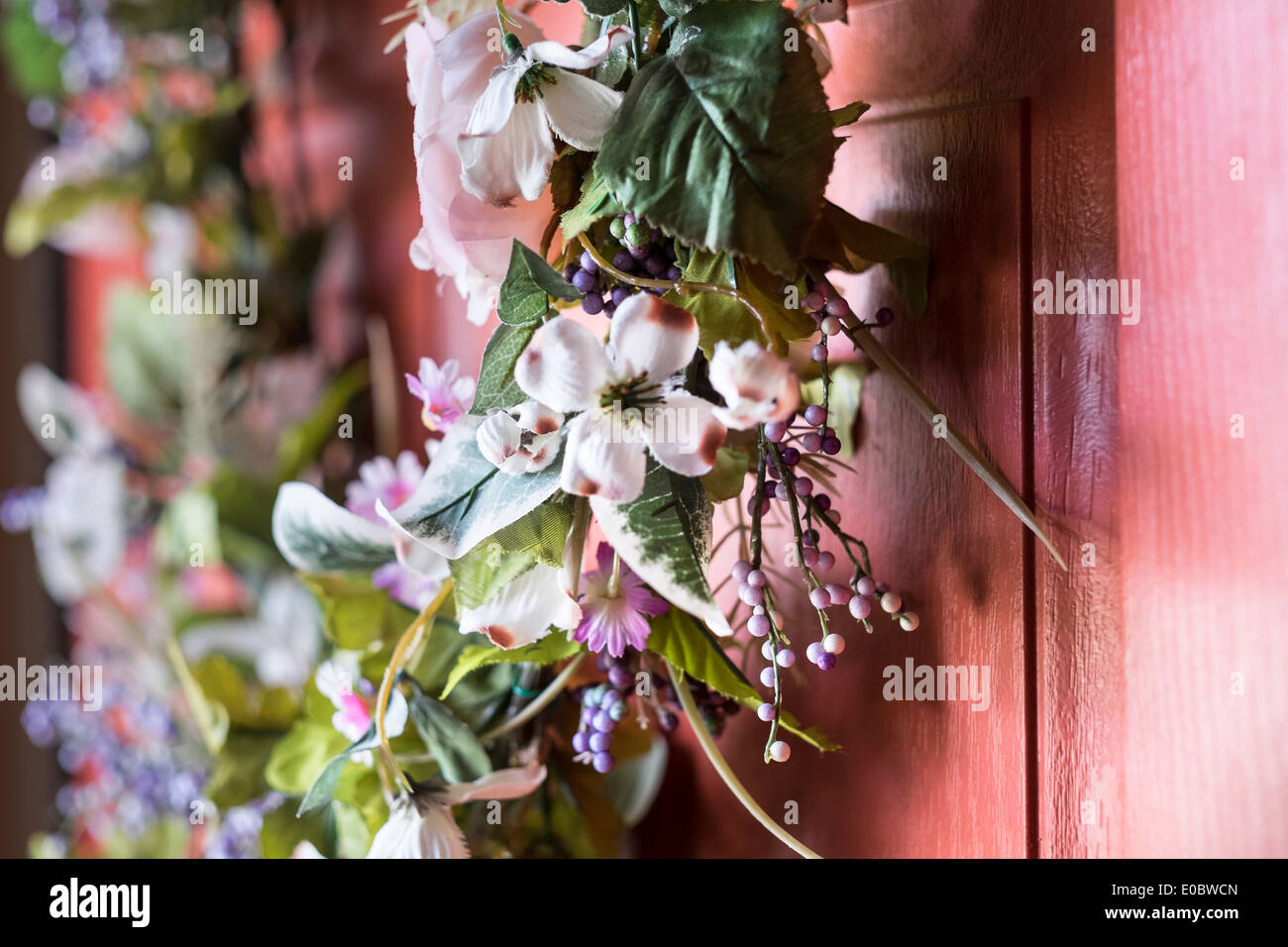Primo piano di una corona di fiori appesi su una porta dipinta soft arancione. Foto Stock