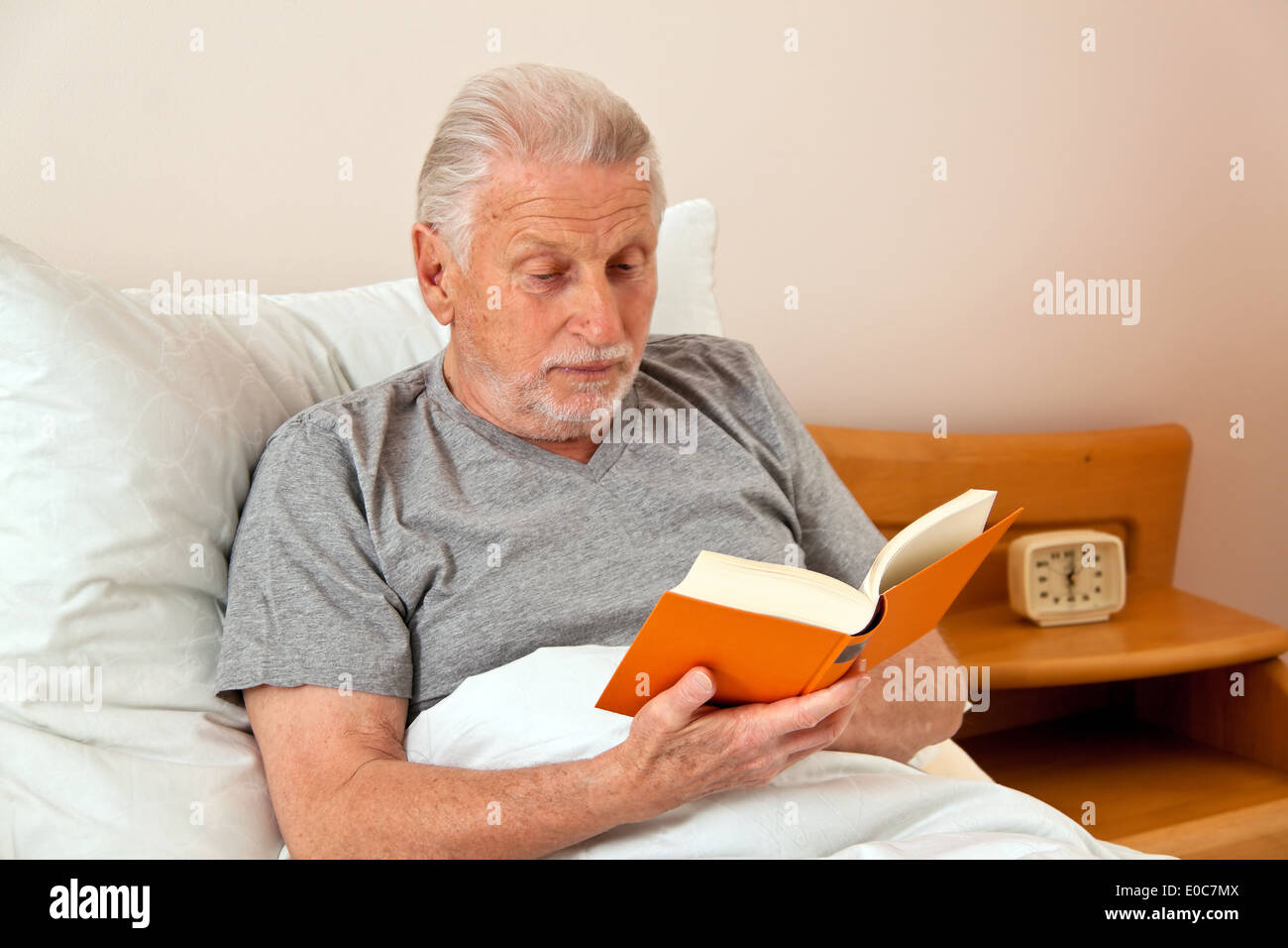 Un boss della vecchia casa di riposo con la lettura del libro nel letto, ein Senior im Altenheim beim Buch lesen im Bett Foto Stock