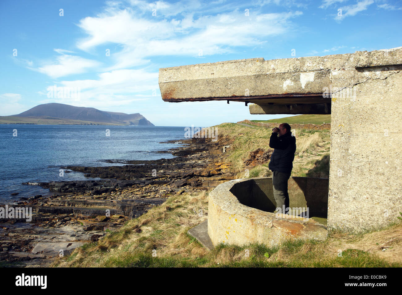 Uomo che guarda attraverso il binocolo e in piedi in uno della guerra di difesa delle strutture costiere vicino a Stromness sulle Isole Orcadi Foto Stock