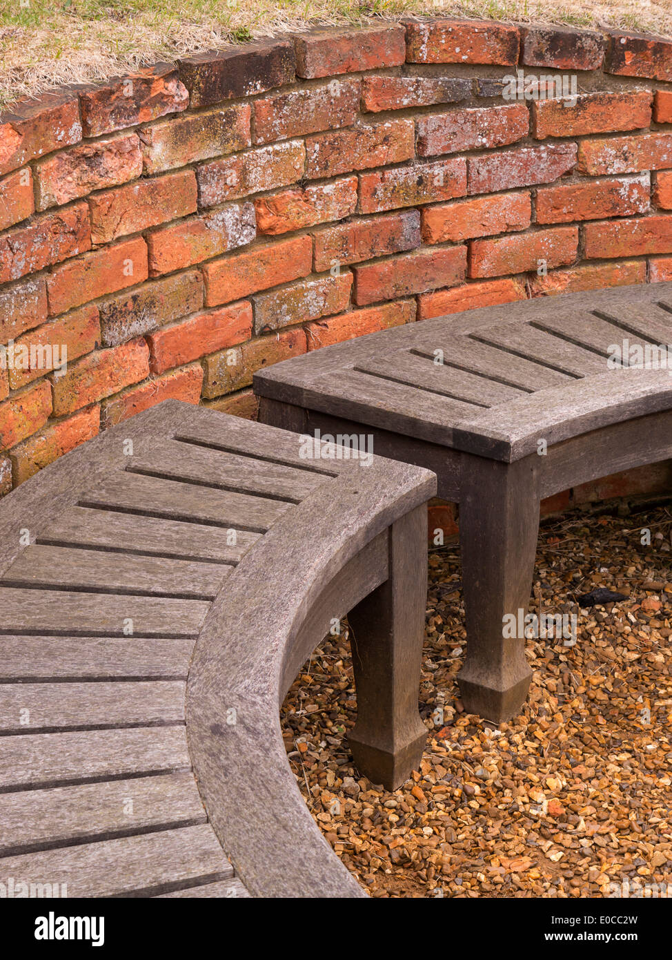 In legno curvato sedile unico e rosso vecchio muro di mattoni, Coton Manor Gardens, Coton, Northamptonshire, England, Regno Unito Foto Stock