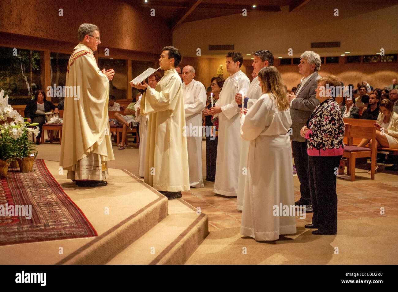 Il parroco di San Timoteo della Chiesa Cattolica, Laguna Niguel, CA, legge il Vangelo ai nuovi membri della congregazione la notte del loro battesimo. Nota vesti bianche e sponsor. Foto Stock
