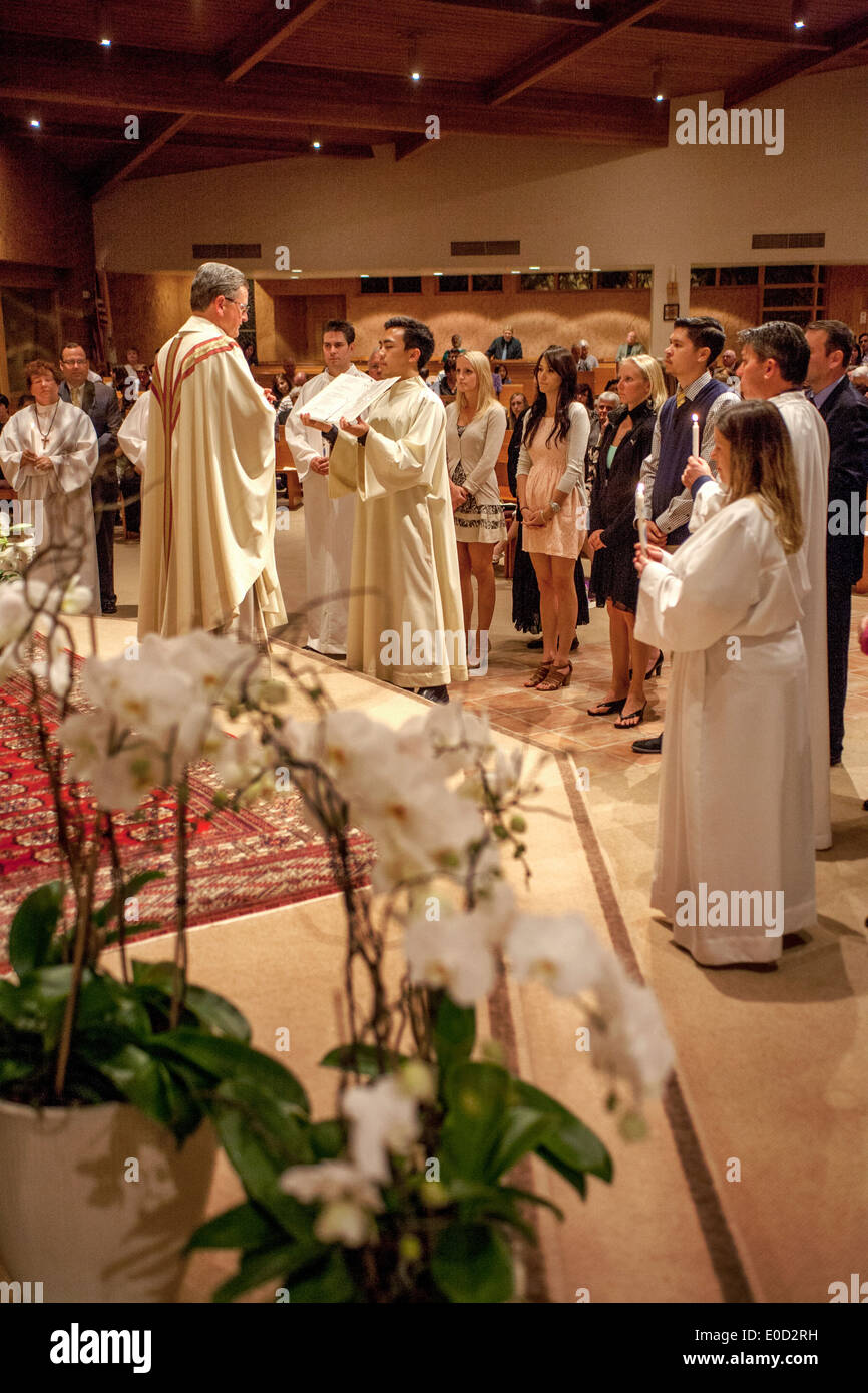 Il parroco di San Timoteo della Chiesa Cattolica, Laguna Niguel, CA, legge il Vangelo ai nuovi membri della congregazione la notte del loro battesimo. Nota vesti bianche e sponsor. Foto Stock