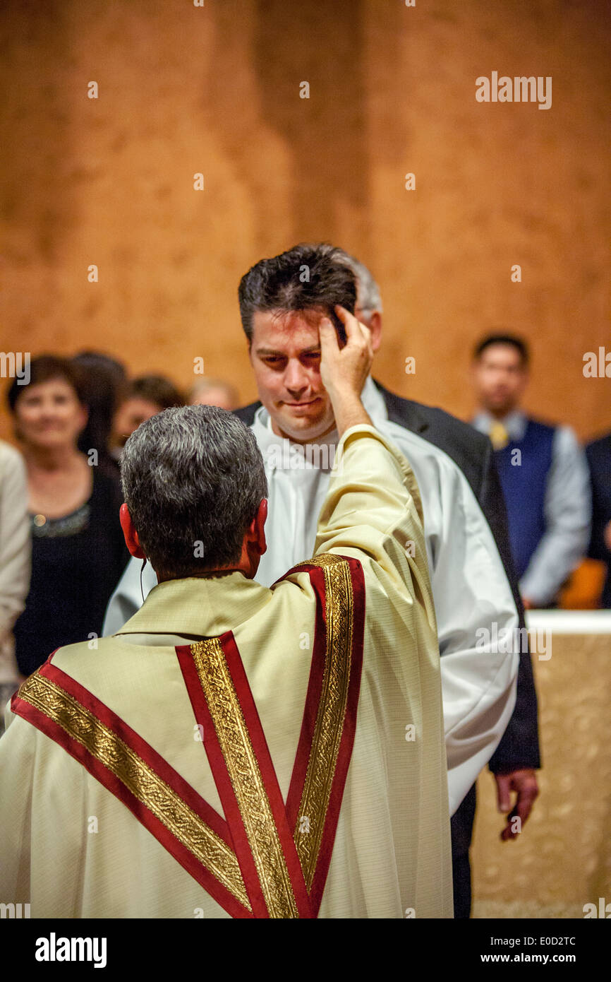 Il parroco di San Timoteo della Chiesa Cattolica, Laguna Niguel, CA, benedice un nuovo membro della congregazione la notte del suo battesimo. Nota tunica bianca. Foto Stock