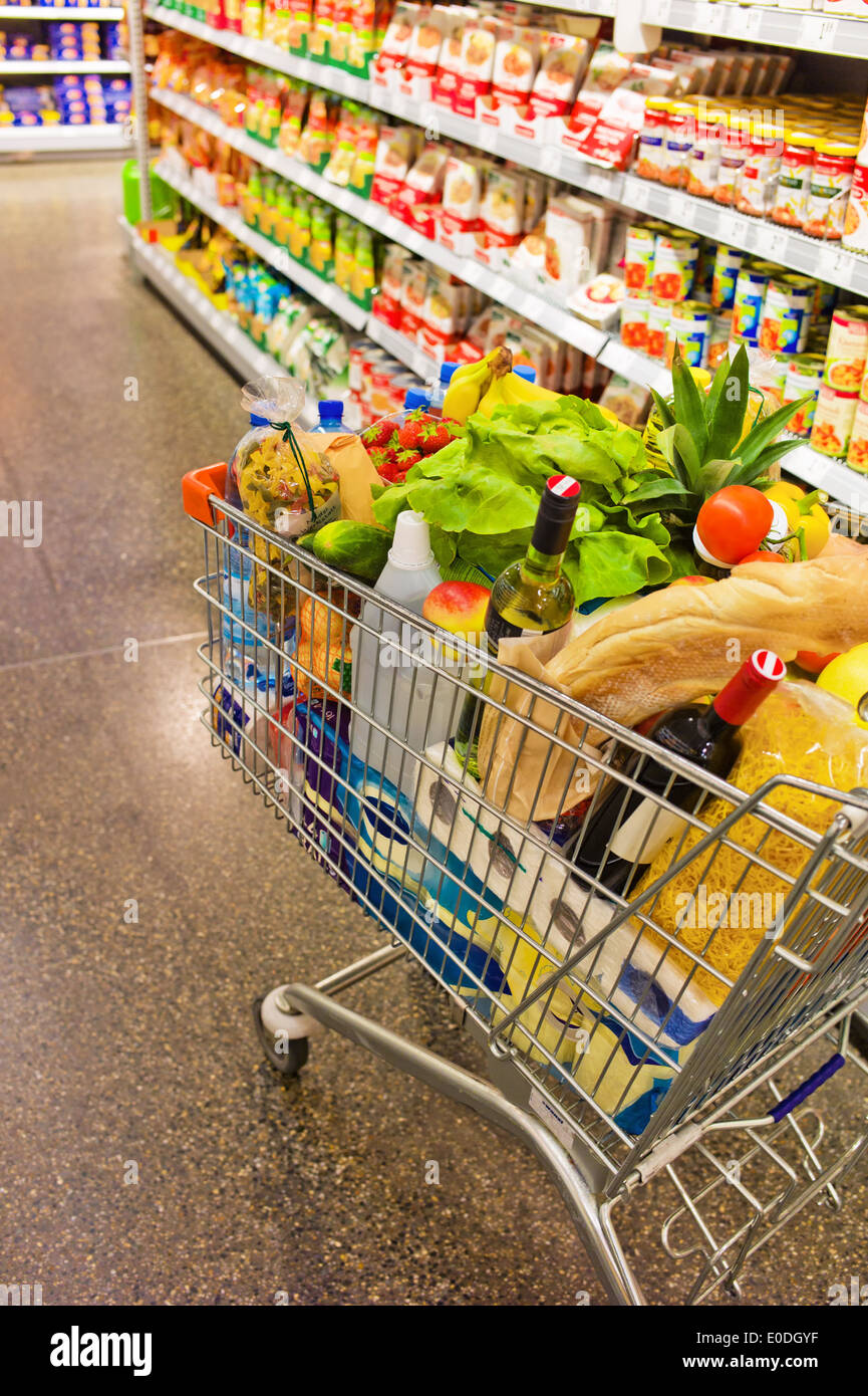 Un carrello di shopping sorge in un modo di un supermercato tra scaffali, Ein Einkaufswagen steht in einem pista eines Supermarktes Foto Stock