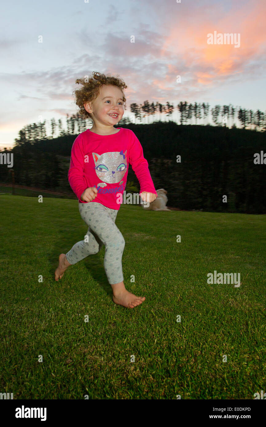 Giovane ragazza sorridente e in esecuzione su una fattoria al tramonto Foto Stock
