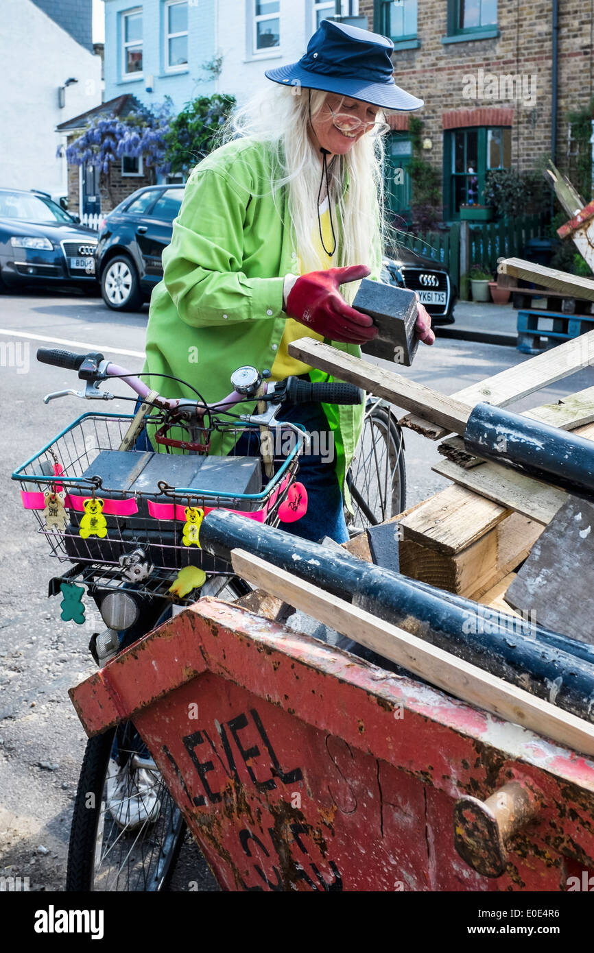 Il riciclo dei materiali da costruzione - senior donna in abiti colorati si sposta mattoni da Skip to decorate Cestino bici per il riutilizzo Foto Stock