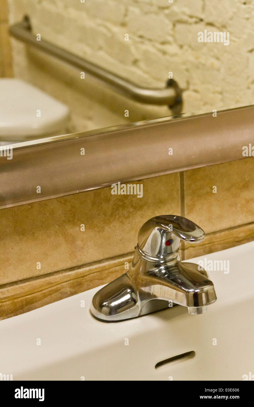Parte di un lavello e rubinetto con un wc e corrimano per i portatori di handicap riflessa nello specchio sopra Foto Stock