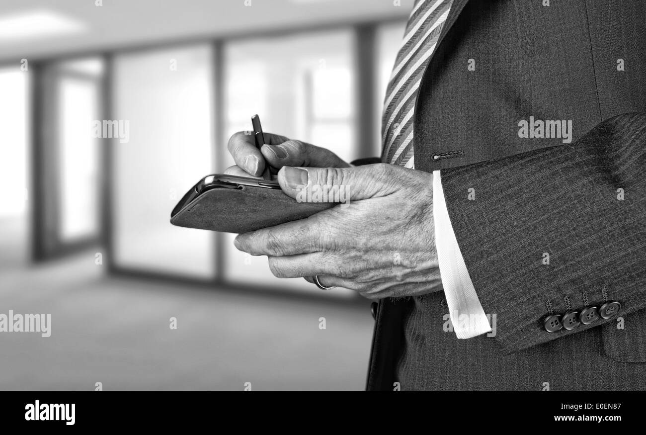 Un imprenditore iscritto un messaggio con uno stilo su un dispositivo elettronico. Foto Stock