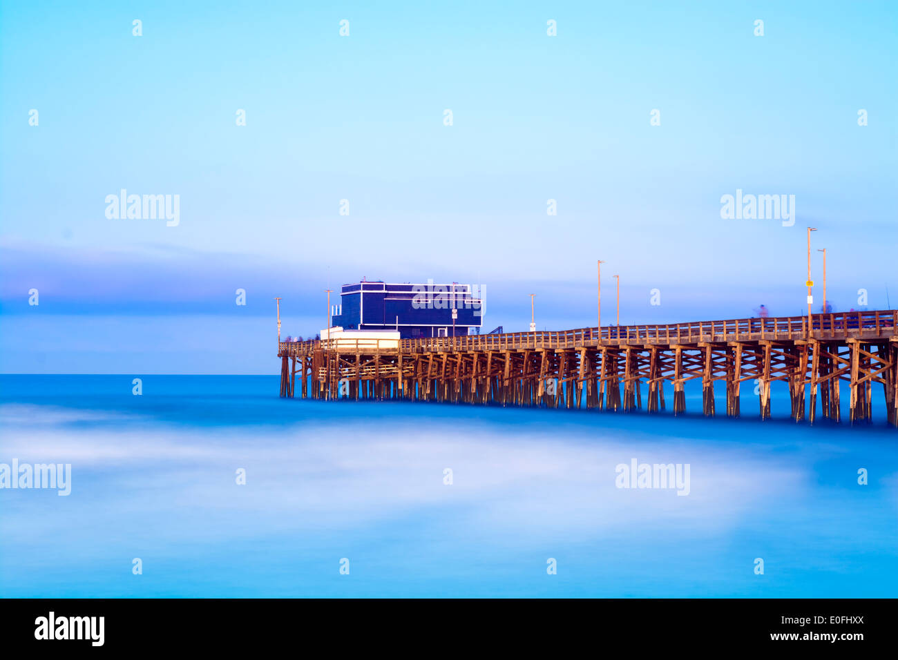 Balboa pier a Newport Beach in California durante il sunrise mostra la struttura di legno del molo e un vibrante, il blu del cielo e del mare. Foto Stock