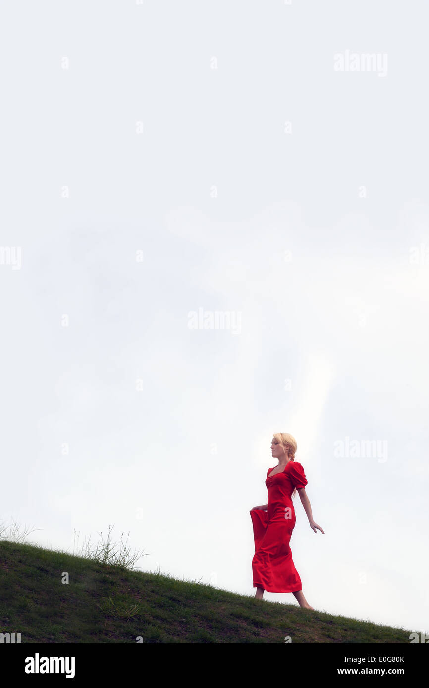Una ragazza in un abito rosso è camminare in salita Foto Stock