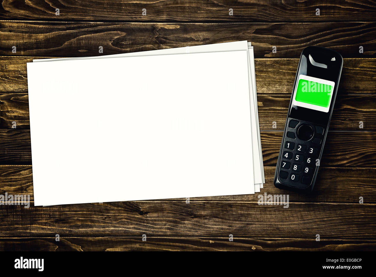 Accesso wireless a un telefono cordless e fogli di carta bianca con copia spazio sul tavolo di legno. Foto Stock