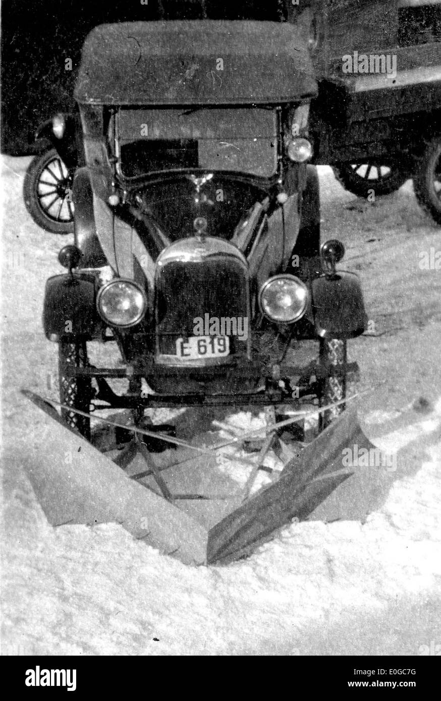 Una spazzaneve che elimina la neve da una strada in inverno, con un veicolo e un paesaggio innevato sullo sfondo. Questa foto mostra le sfide legate al mantenimento delle rotte di trasporto durante le dure condizioni invernali. Foto Stock