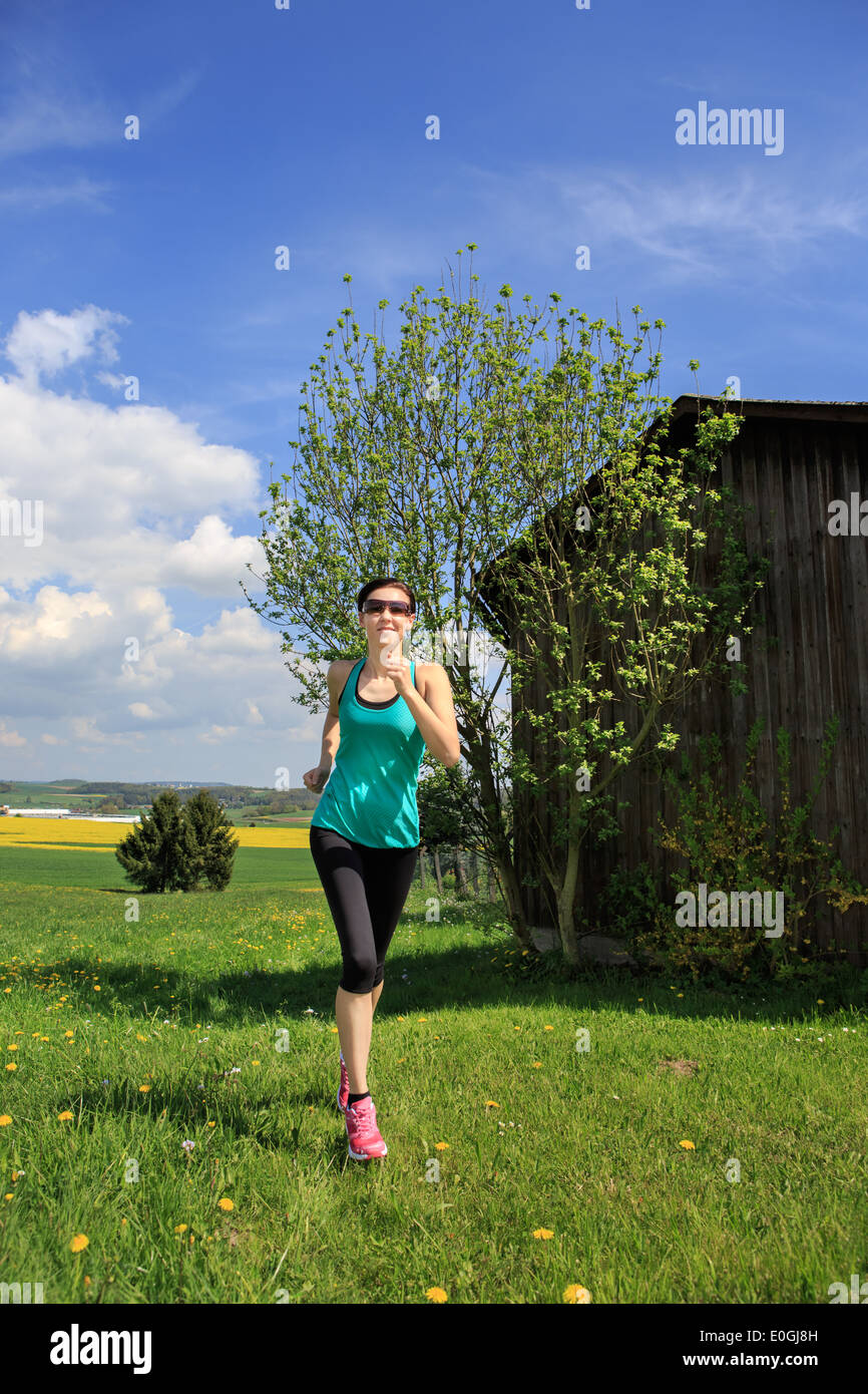 Donna jogging attraverso i campi in primavera Foto Stock