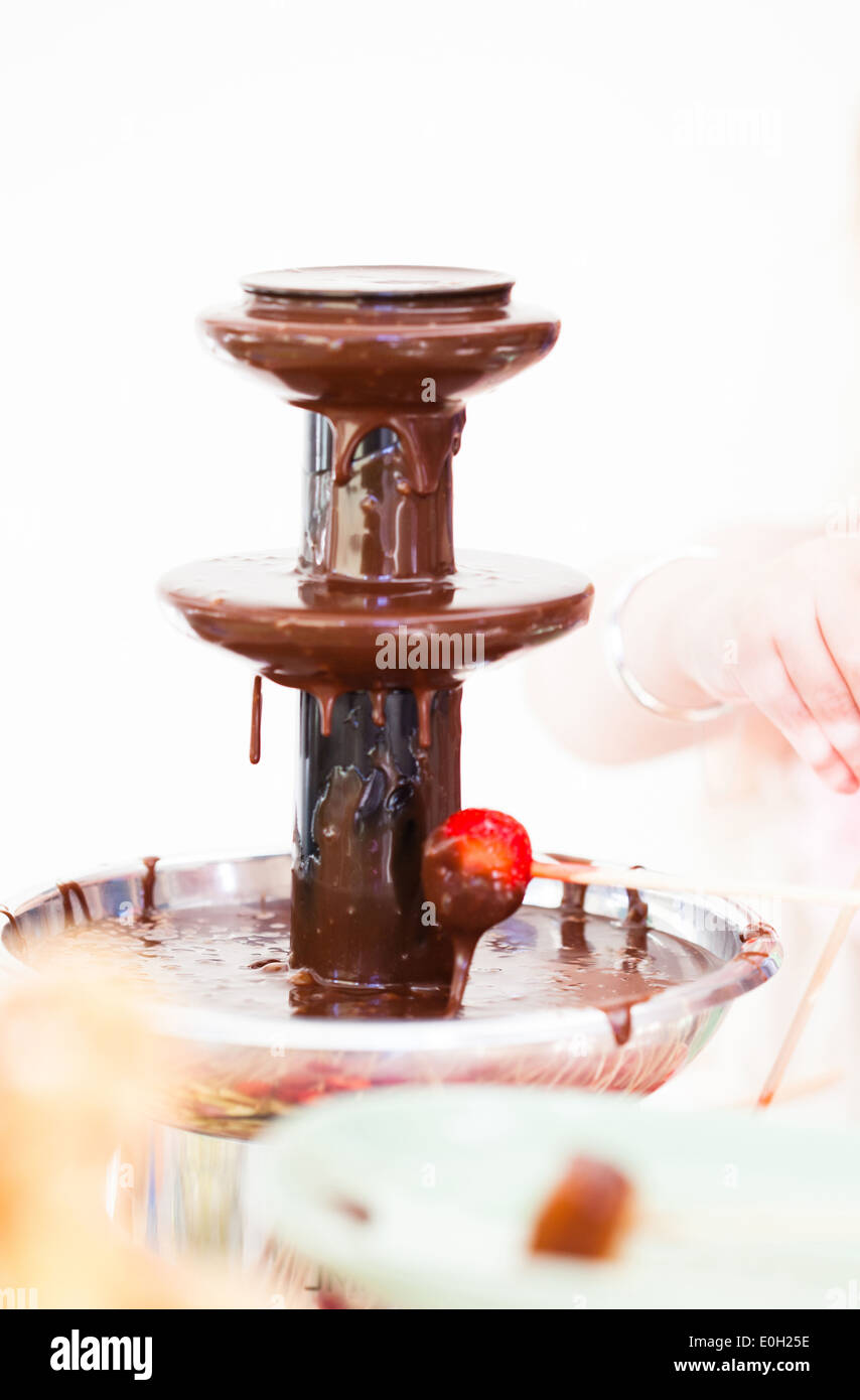 Primo piano della fonduta di cioccolato fontana con una fragola su stick Foto Stock