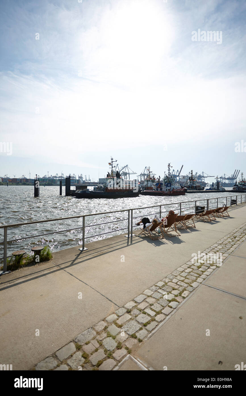 Persone in sedie a sdraio a guardare le barche di traino a Neumuehlen Pier, dal porto di Amburgo, Germania Foto Stock