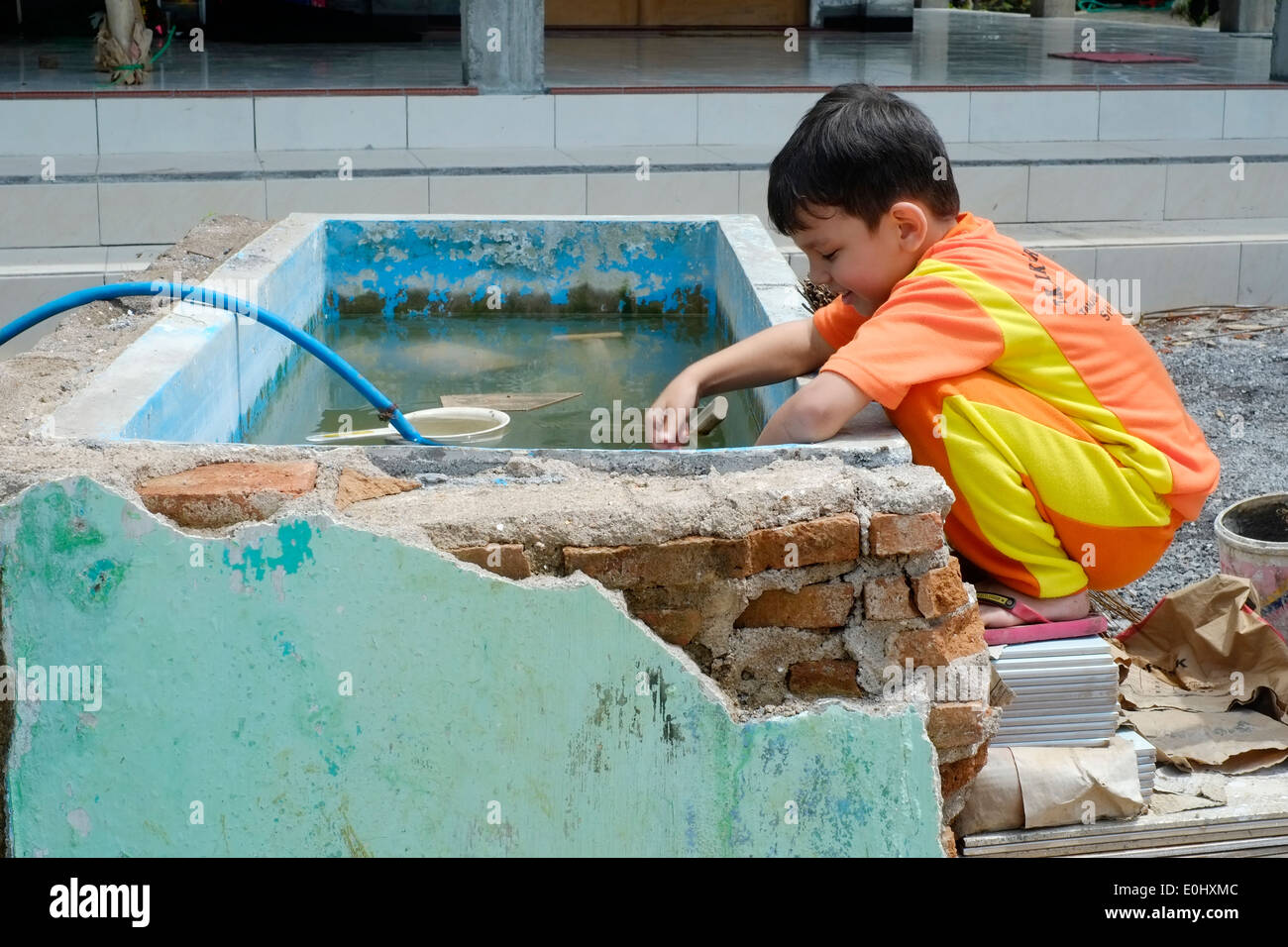 Giovane ragazzo locale giocando accanto a un trogolo di acqua su un sito di costruzione in Giava Est Indonesia Foto Stock