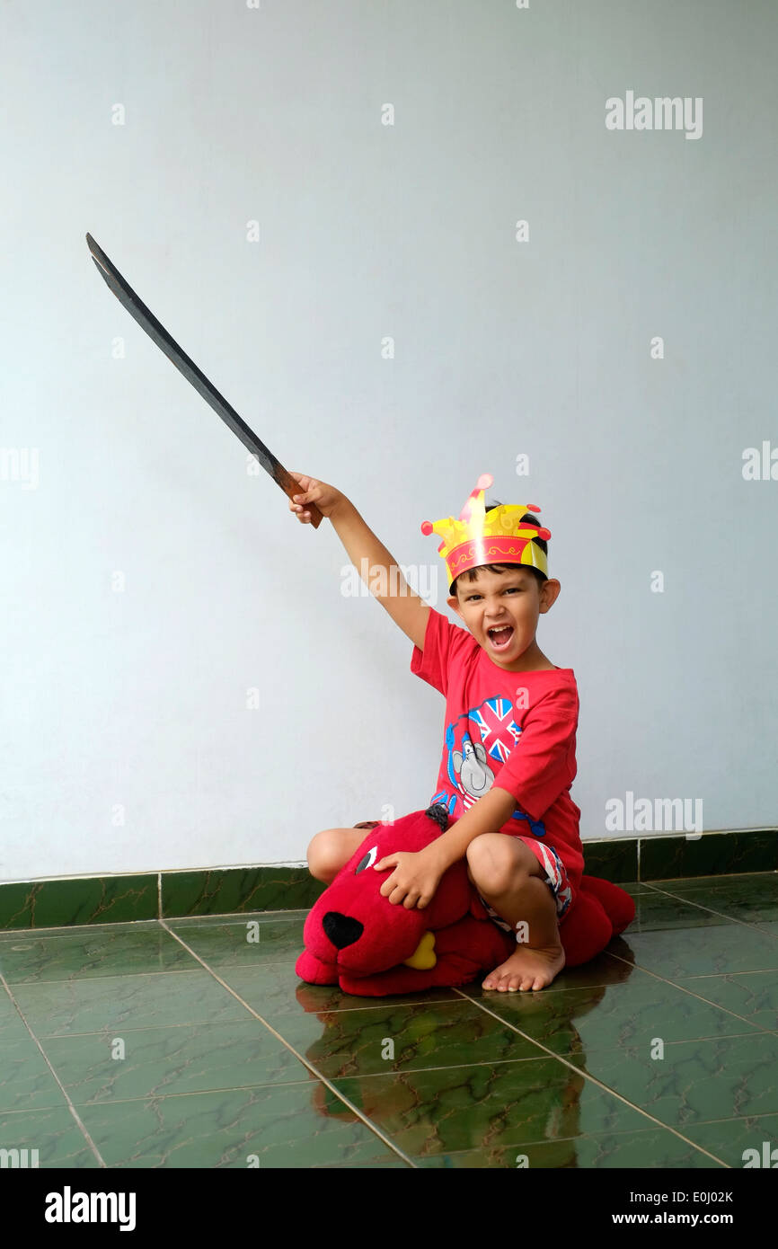 Little Boy con la spada e la corona seduti sul cane giocattolo a giocare a essendo un cavaliere Foto Stock