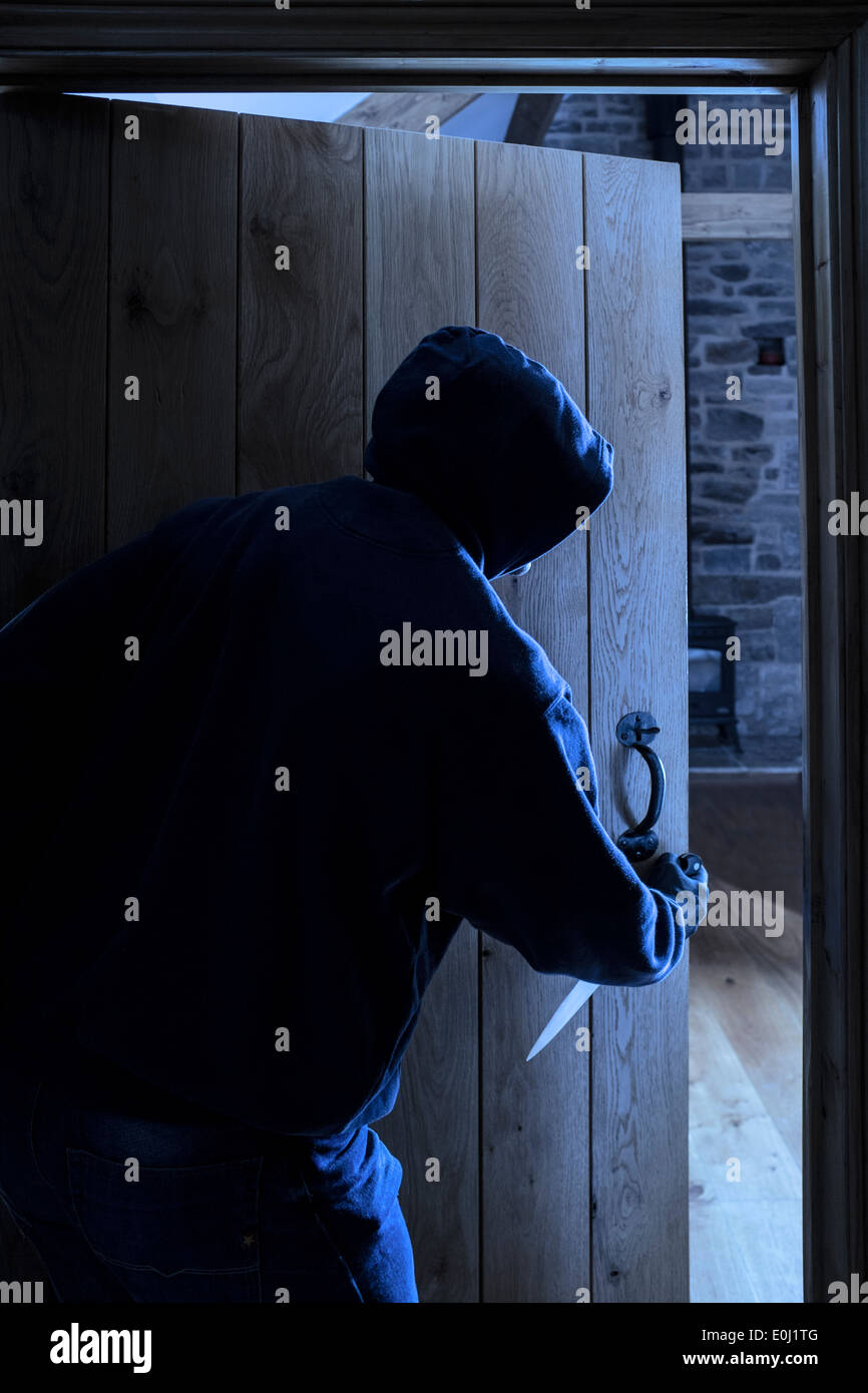 Un anonimo maschio con cappuccio portando un coltello di entrare in una stanza. Foto Stock