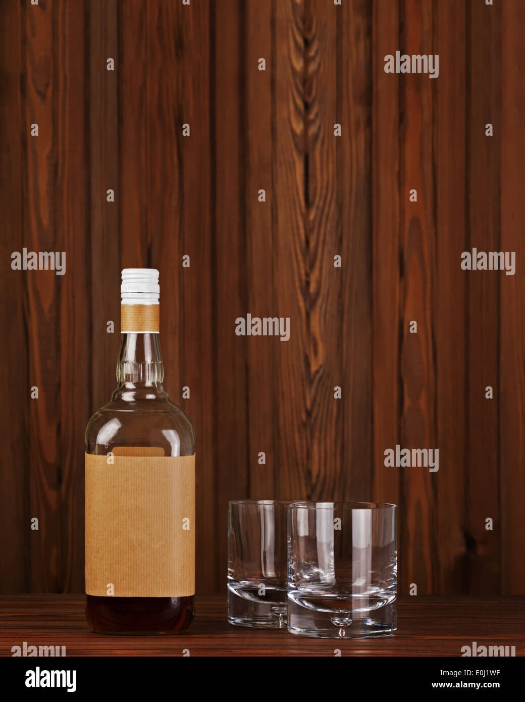 Due bicchieri con ghiaccio per whiskey e bottiglia sul legno scuro dello sfondo. Foto Stock