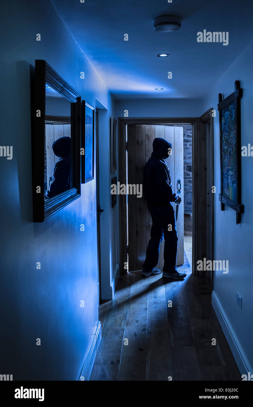 Un anonimo maschio con cappuccio che porta una lama di entrare in una camera che porta un coltello. Foto Stock