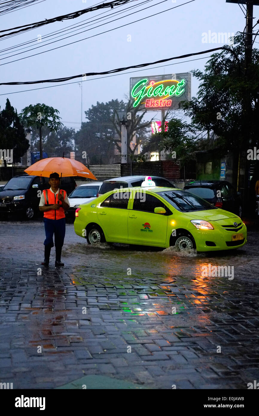 Parcheggio auto attendant con ombrello durante un diluvio di piogge monsoniche scurisce il tardo pomeriggio sky a malang indonesia Foto Stock