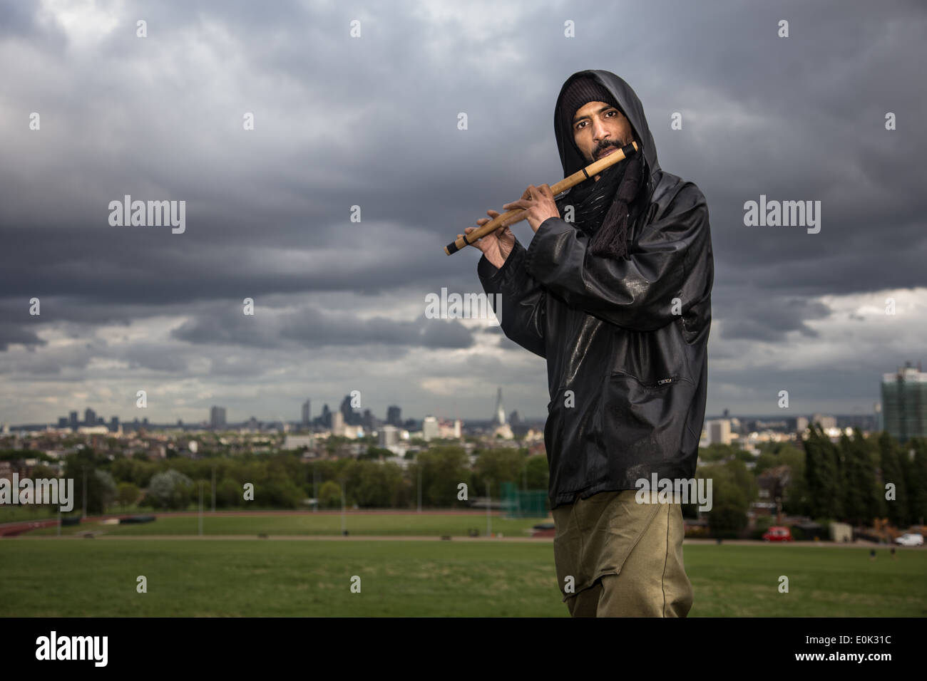 Razza mista uomo suonare il flauto in erba lunga su Hampstead Heath indossa velo e nero camicia lucida Foto Stock