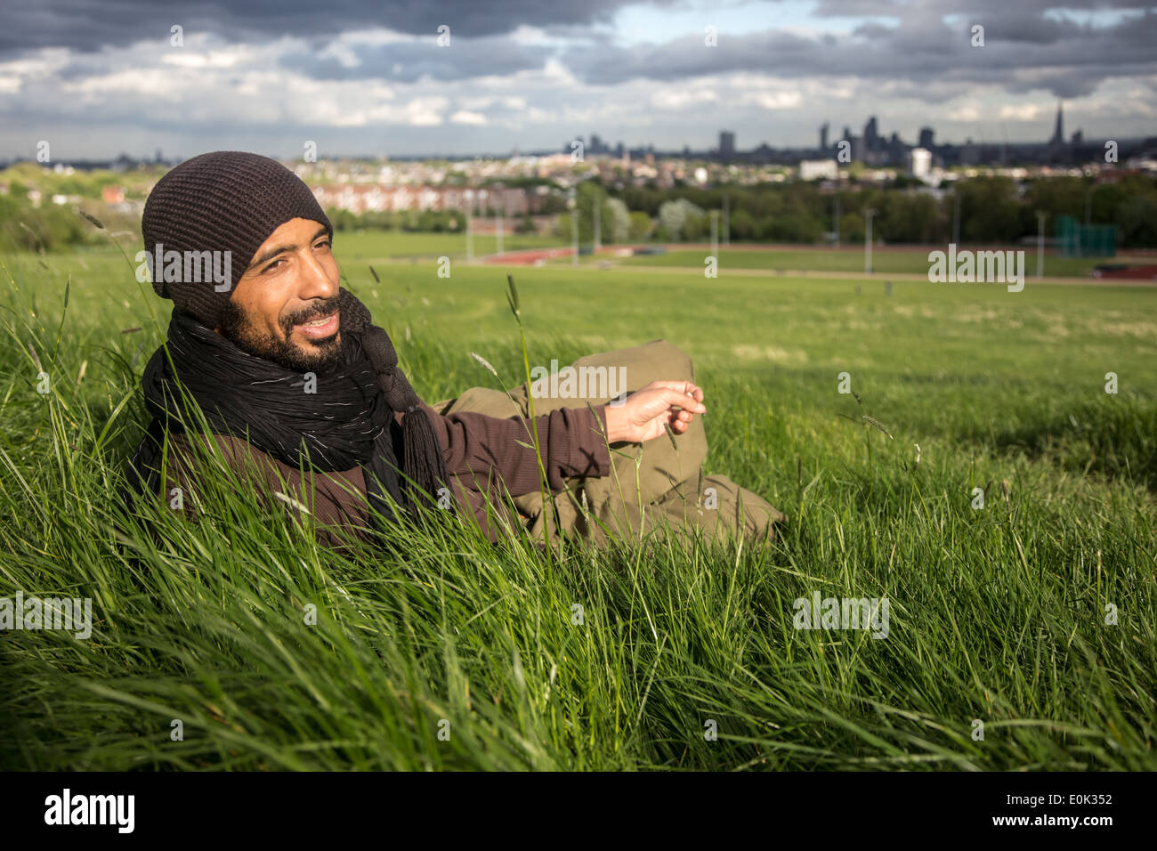 Razza mista uomo rilassante in erba lunga su Hampstead Heath indossa velo e vestiti larghi Foto Stock