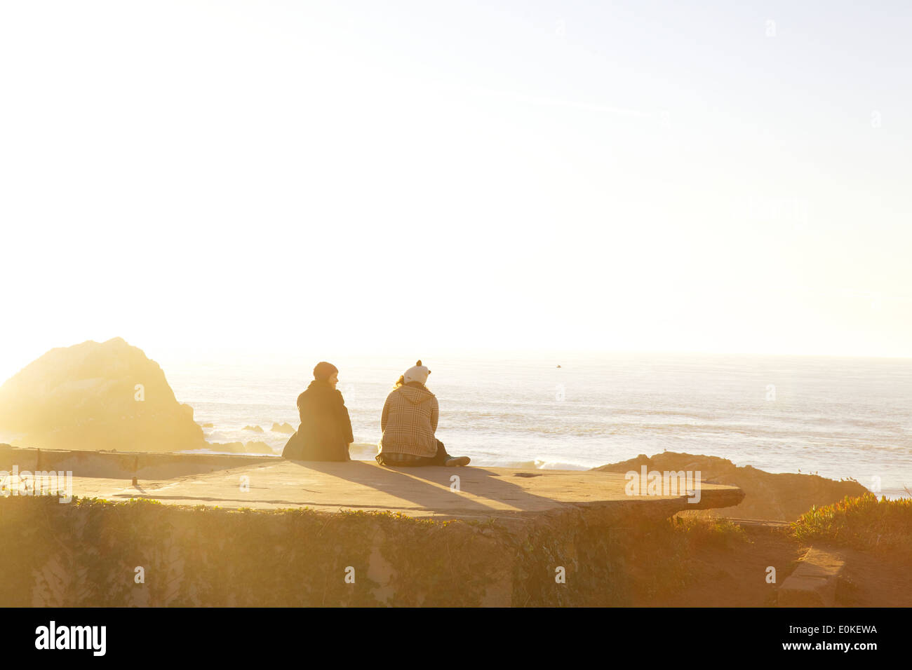 Due giovani amici di sesso femminile sedervi al sole presso il lungomare presso i bagni Sutro a Lands End in San Francisco, California. Foto Stock