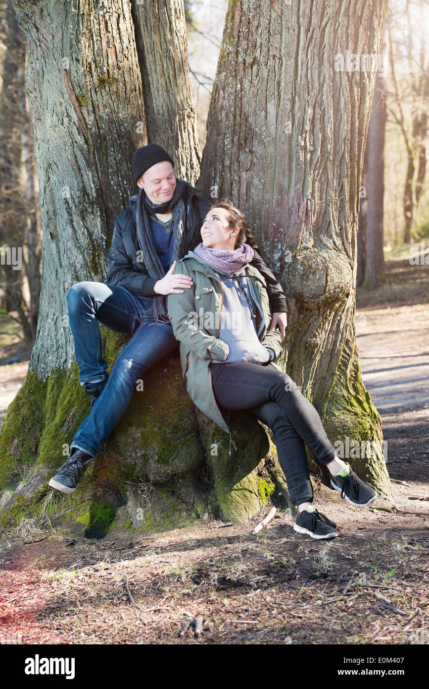 Coppia felice in natura l'impostazione. Giovane uomo e donna seduta da un albero, riposo durante una passeggiata nei boschi. Foto Stock