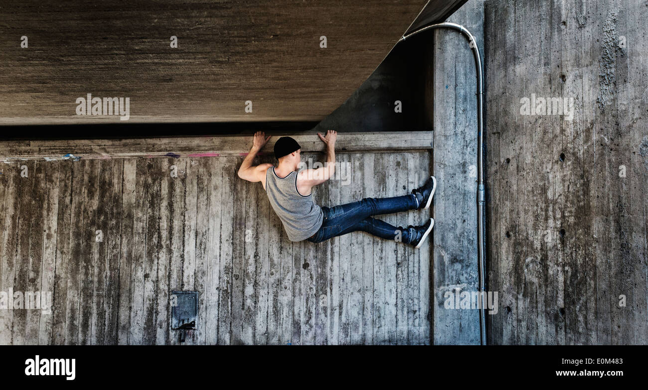 Giovane uomo appeso in una parkour spostare sul muro di cemento scena urbana con il momento dello stile di vita dei giovani pieni di energia e forza Foto Stock