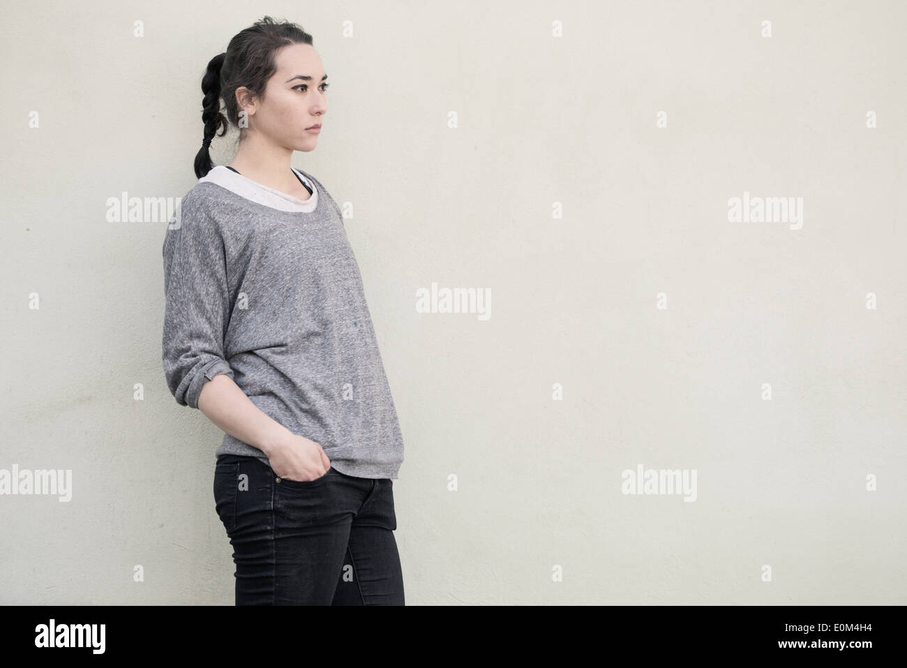 Ritratto di giovane donna ispanica in piedi nella parte anteriore della parete. Malinconici espressione e guardando lontano. Foto Stock